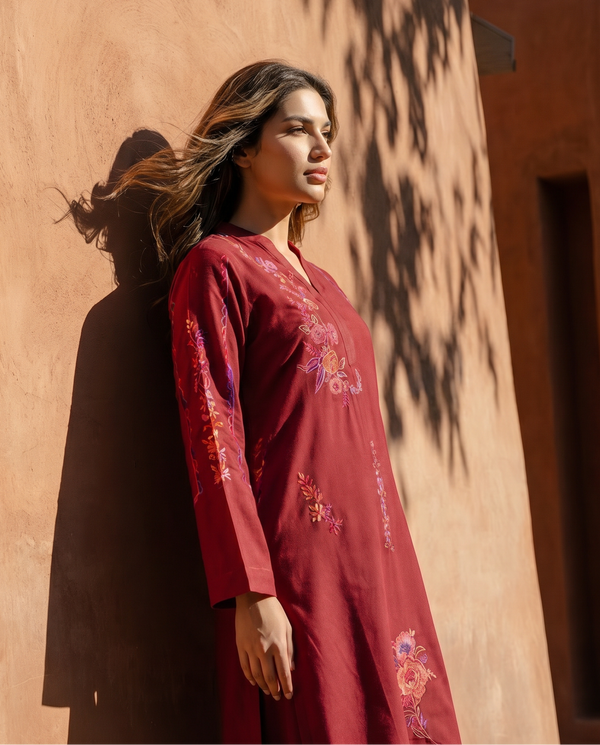 Woman in a red embroidered dress standing against a warm-toned wall.