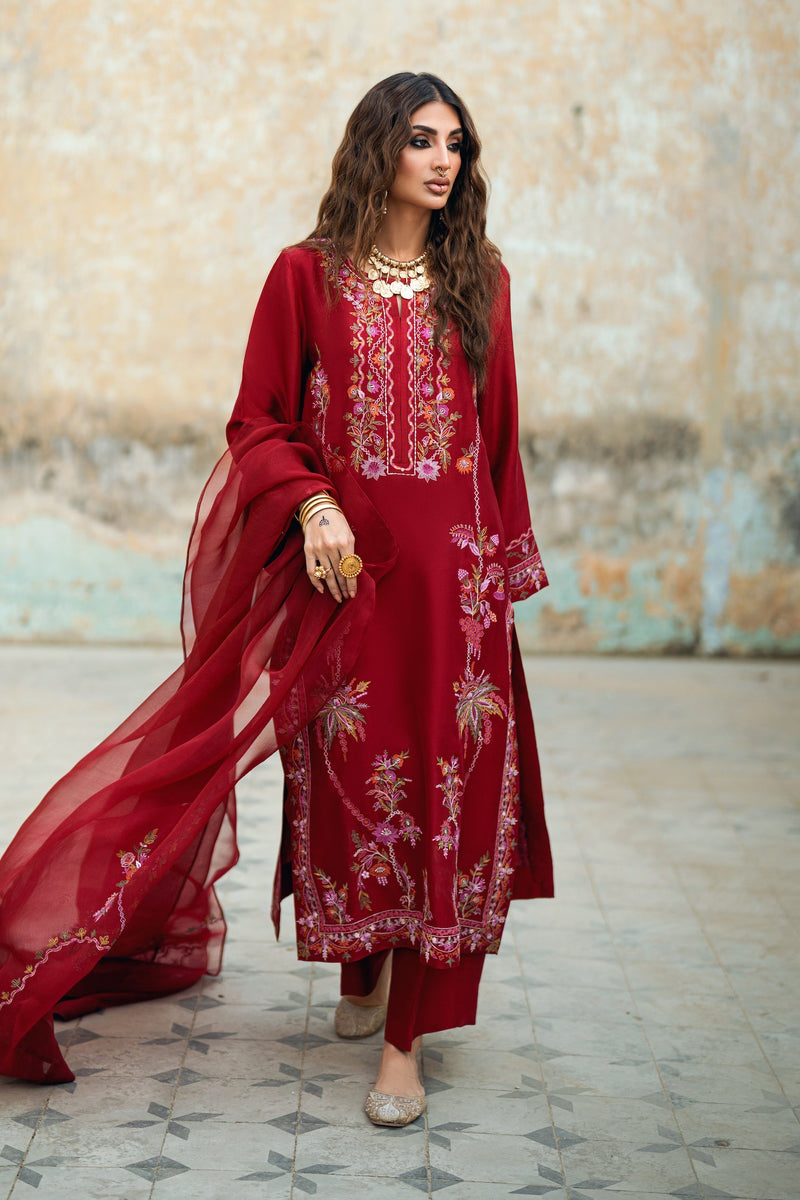 Woman in a red embroidered outfit standing against a textured wall.