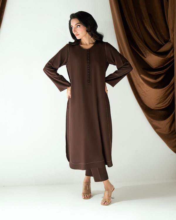 Woman wearing a brown dress standing in front of brown curtains on a white background