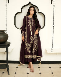 A woman modeling a long, dark plum embroidered kurta with beige floral patterns, standing in front of a white wall with a black arched frame.